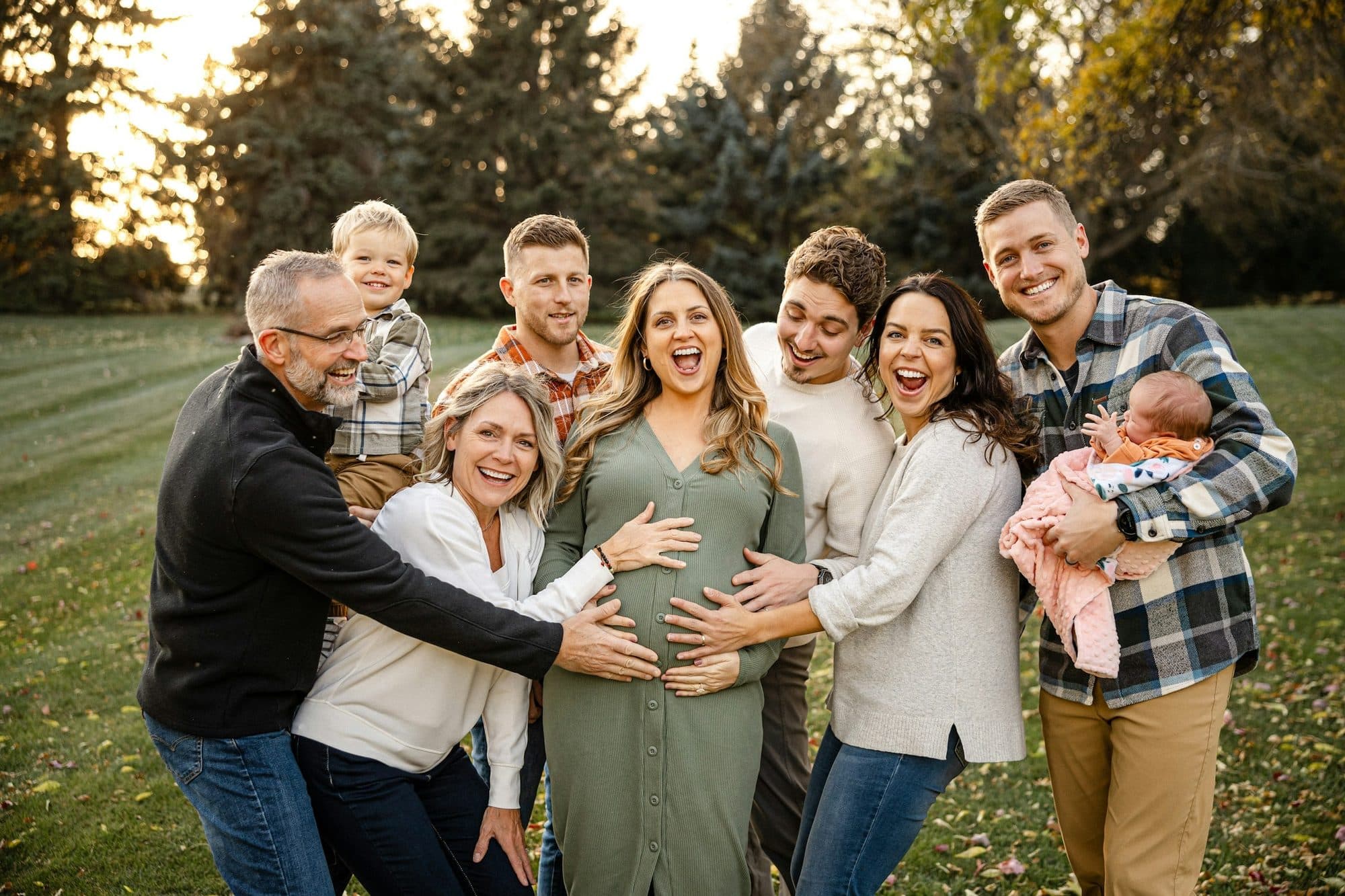 Four generations of a family laughing together on a lawn at sunset
