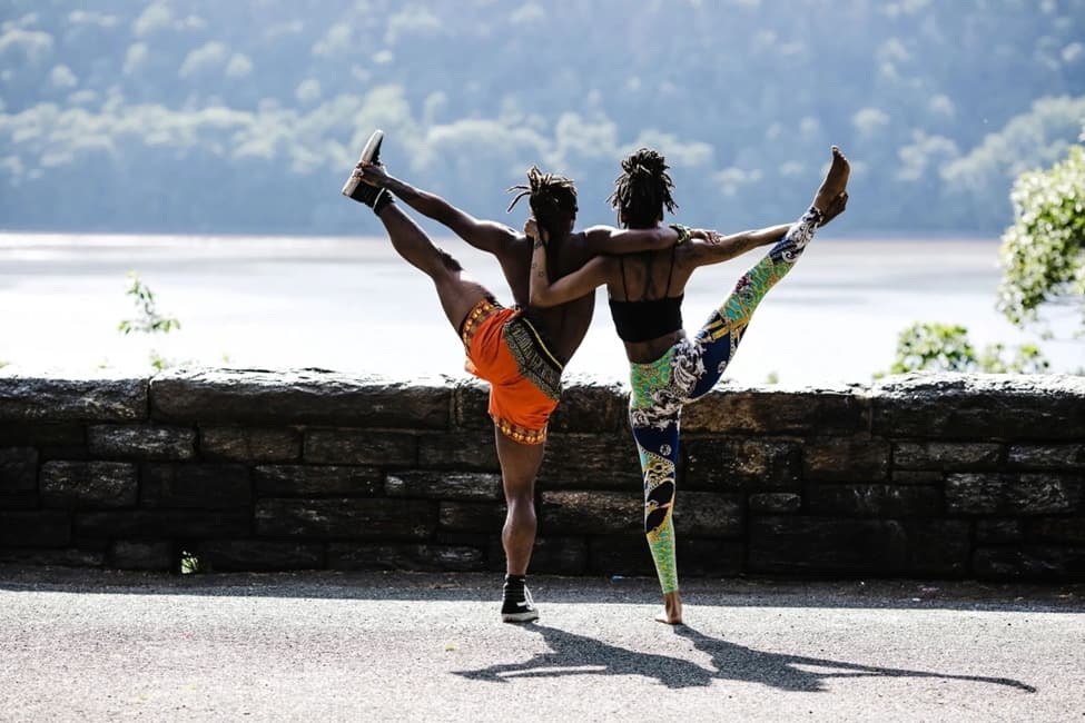Two people balanced on one leg in a dancer pose on a path above the water